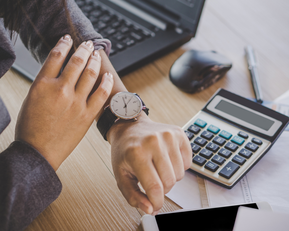 Person checking their watch with a calculator in the background.